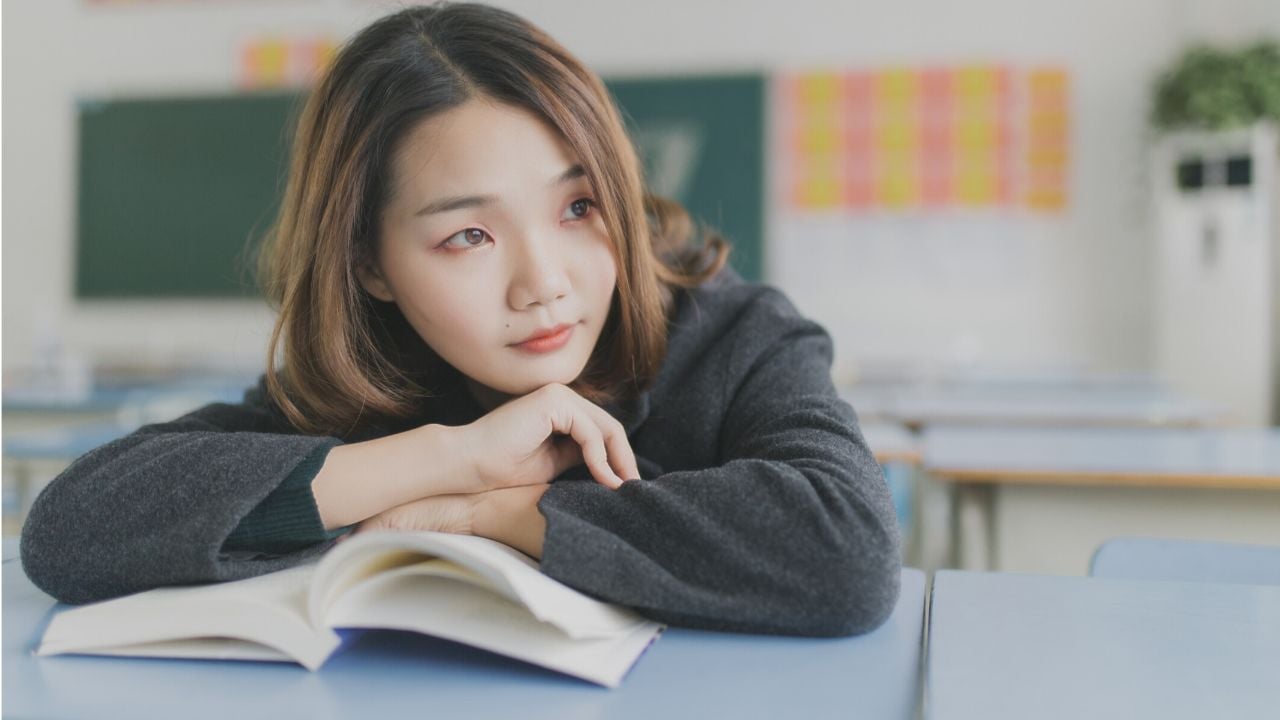student in a gray sweater leaning on an open book